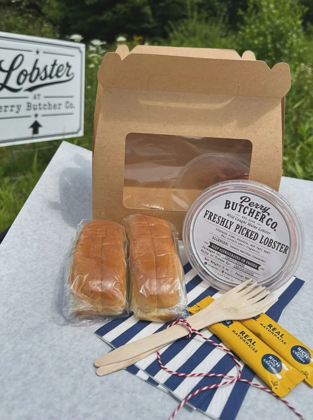 Perry Butcher Co. Lobster Roll Kit package — the kraft carrier box with a labeled tub of freshly picked Maine lobster meat, two brioche buns, mayonnaise and wooden utensils